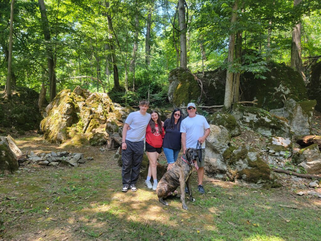 Family exploring the moss-covered boulders with their dog at Timber Valley Retreat during a Cabin Retreat in Western Maryland surrounded by peaceful woodland scenery.