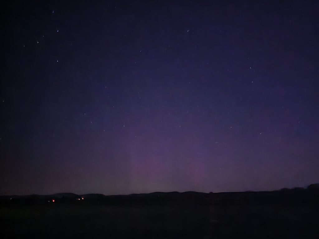 Faint Northern Lights glow along the horizon above Timber Valley Retreat beneath a star-filled night sky