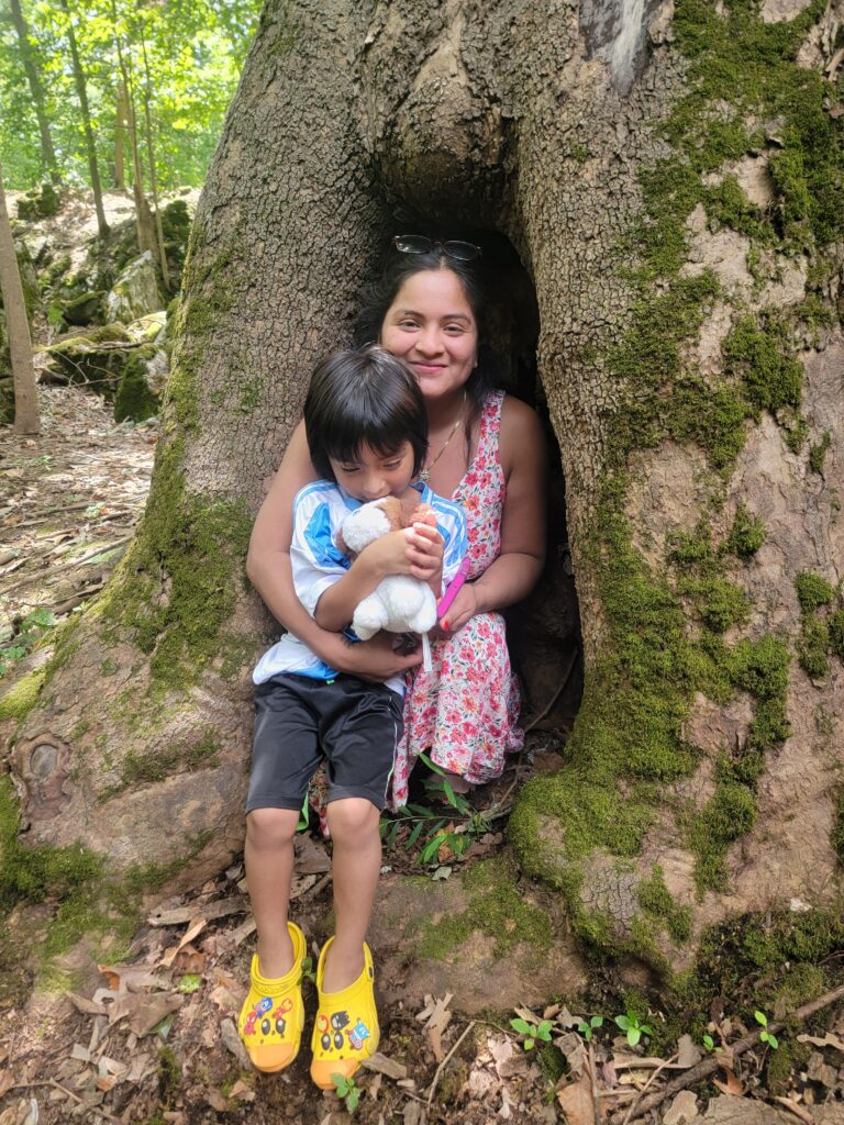 Mother and child exploring a hollow tree at Timber Valley Retreat in Western Maryland surrounded by moss-covered rocks and woodland.