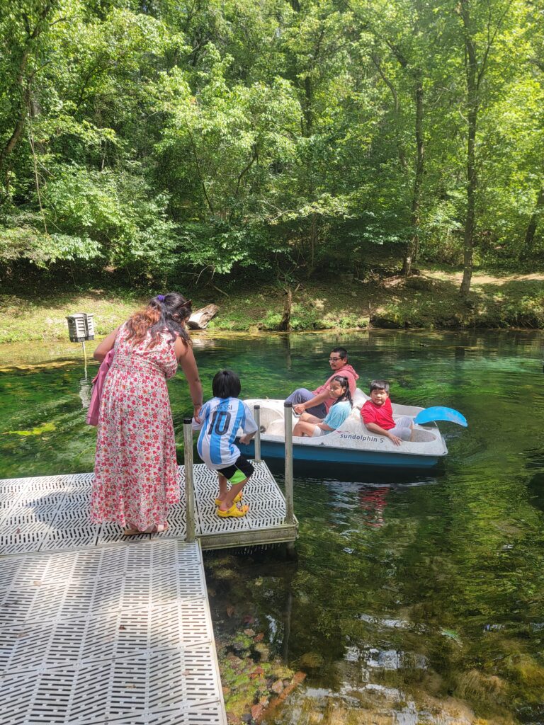Family riding a pedal boat together on the spring-fed pond at Timber Valley Retreat surrounded by Maryland woodland.