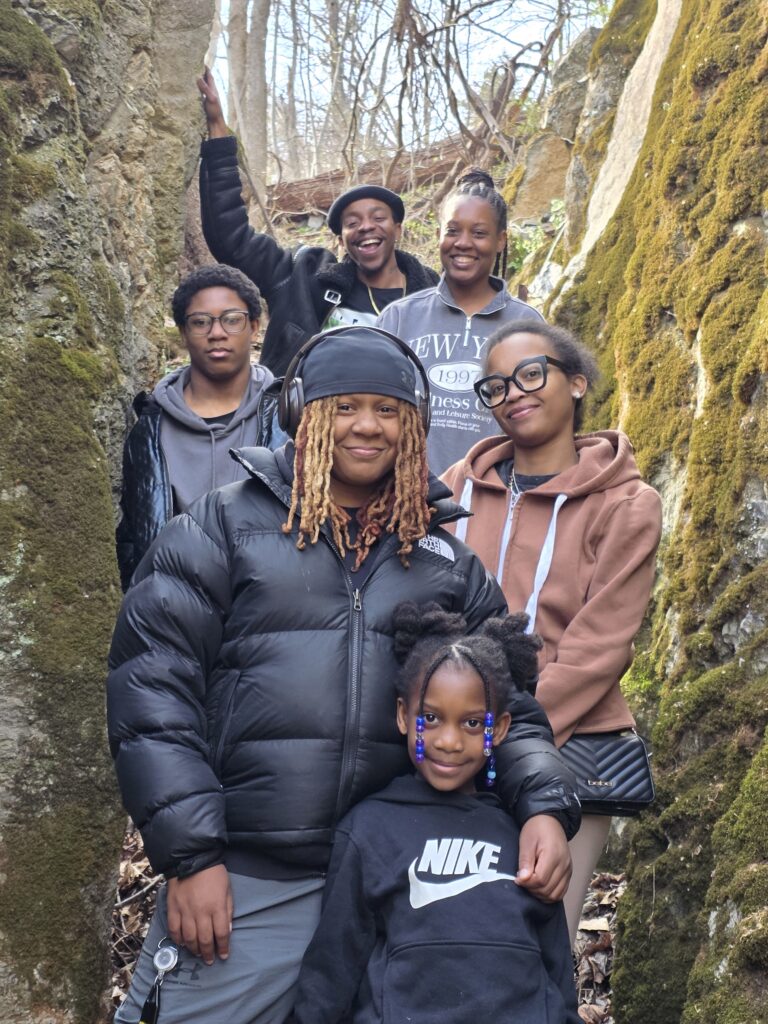 Family exploring a narrow passage between moss-covered rock formations at Timber Valley Retreat in Western Maryland.