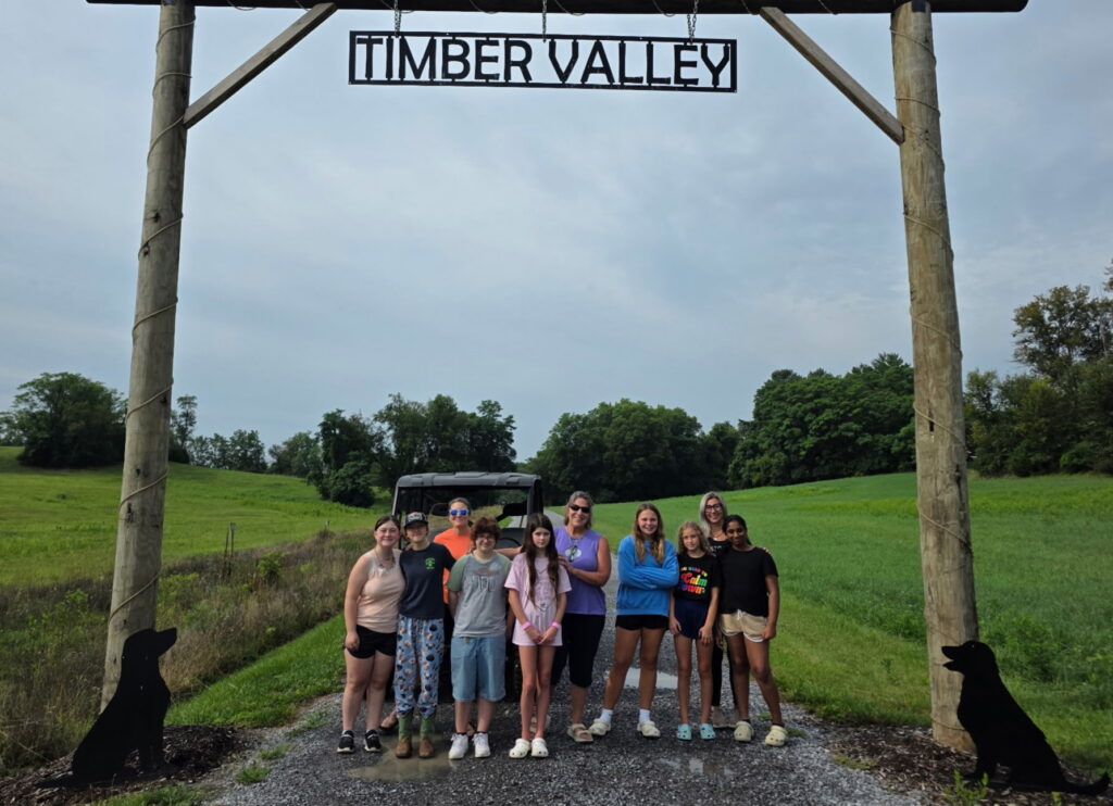 Girl Scouts posing beneath the Timber Valley sign during a group cabin getaway in Maryland