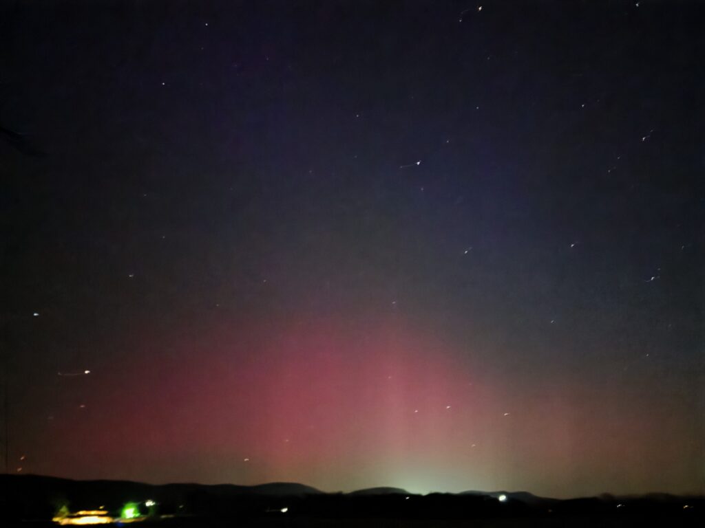 Northern lights glowing above the hills with stars visible at Timber Valley Retreat