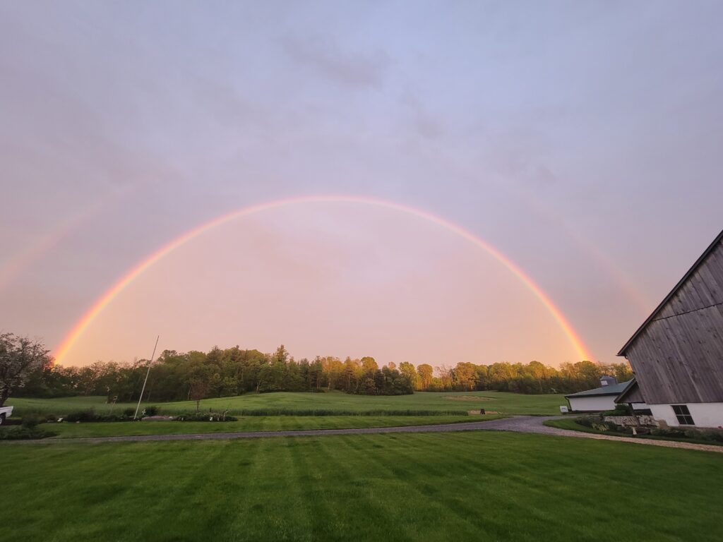 Western Maryland Rainbow arching over Timber Valley Retreat with the barn, rolling hills, and peaceful countryside after a summer rain.